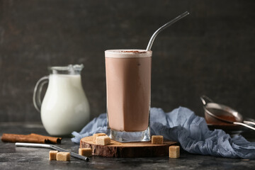 Glass of cold cocoa drink with sugar cubes and cinnamon sticks on grey grunge background