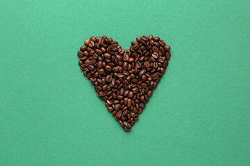 Heart made of coffee beans on green background