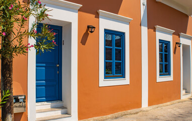 Close up of a colorful neoclassical house, blue windows on an orange wall, Symi town on Symi island, Greece