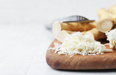 Grated horseradish, grater and fresh roots on white tiled table, closeup. Space for text
