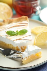 Slice of tasty lemon meringue tart with mint served on blue table, closeup