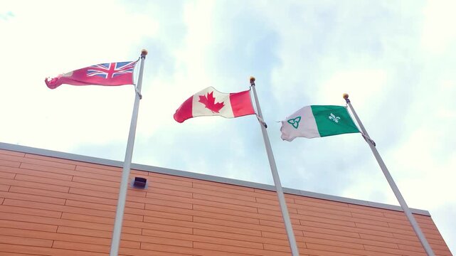 Three flags representing Ontario, Canada, and Franco-Ontarian communities fly high against a bright sky, symbolizing unity and cultural diversity.