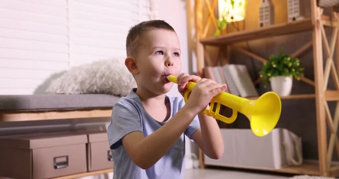 Cute little boy playing toy trumpet at home