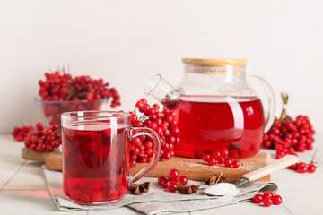 Glass cup and teapot of hot viburnum tea with star anise on white tile table against light wall
