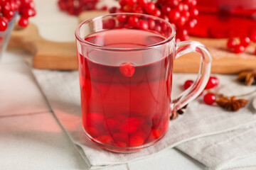 Glass cup of hot viburnum tea on white tile background