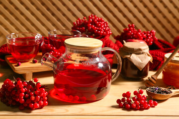Glass cups and teapot of hot viburnum tea with jars on wooden background