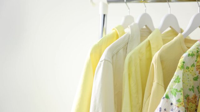 Different stylish clothes hanging on rack near white wall indoors, closeup. Camera moving left