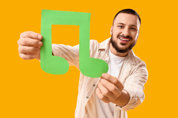Young man with paper music note on yellow background
