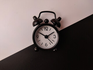 The small black analog alarm clock on a black and white background