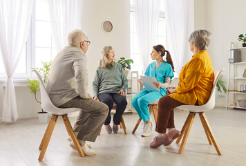 Group of elderly seniors sitting in a circle in nursing home with friendly young nurse and...