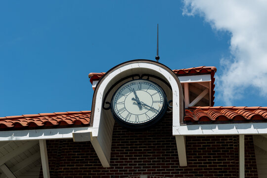 An exterior analog clock with a white background and long black arms. The time on the clock is 11:20. The clock has numeric numbers for markers.  The round clock is on the clay tile roof of a building