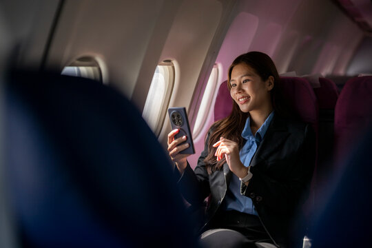 Asian businesswoman traveling on airplane using smartphone