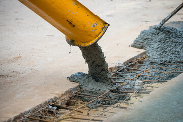 Wet concrete being poured from a yellow chute onto steel reinforcement bars at a construction site