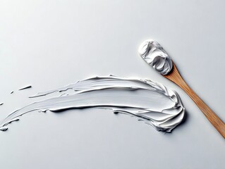 A dollop of thick white cream is swirled on a wooden spoon, with a smear of the same cream creating an abstract pattern on a light surface.