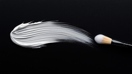 A makeup brush is shown applying a thick, white cream in a sweeping motion against a dark background.