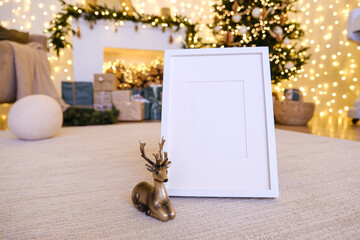 Vertical white picture frame display with blank area, deer figurine on beige carpet with bokeh Christmas light background for holiday promotion.