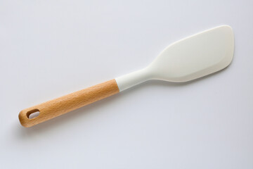 A closeup, top-down studio shot of a modern white silicone spatula with a wooden handle, isolated on a clean white background.