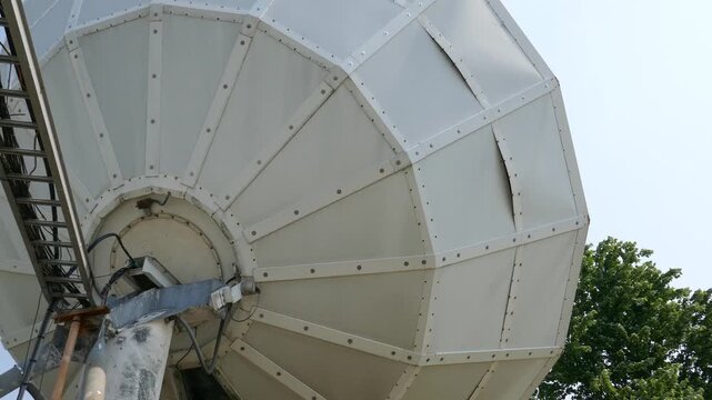 Large satellite dish close-up with trees moving in background