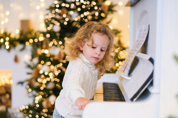 Little caucasian girl playing piano during Christmas. Happy kid learning music in holiday decorated room. Childhood and festive season concept.