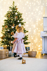 Little girl playing with wooden toy deer by Christmas tree. Kid enjoying festive holiday season at home. Childhood magic and winter celebration.