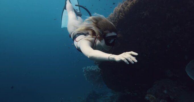 Freediver woman glides in blue ocean. Woman swimming underwater near Japanese wreck in Bali