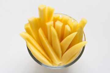 A view of raw, peeled potato strips or sticks in a clear glass bowl, ready for frying or roasting, isolated on a white background.