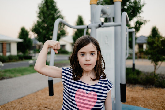 Portrait of a strong young girl looking at the camera, flexing her right bicep muscle after exercising at an outdoor gym; Melbourne, Victoria, Australia