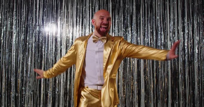 One, two, three, four lets start. Funny overjoyed man in golden stylish suit dancing and moving around, enjoying favourite music, foolishing around, spending free time during party celebration