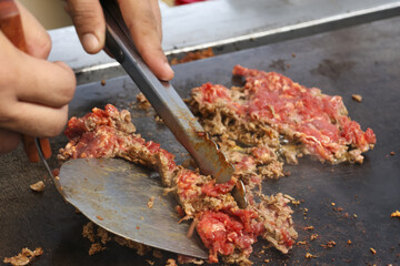 Close up of chef cooking and chopping sizzling ground beef with spatula on hot griddle. delicious meat preparation for meal at street food stall shows an appetizing process