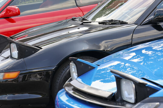 Nostalgic collection of blue, black, and red vintage sports cars parked in row. Close up on shiny automotive bodies and classic pop up headlight design from nineties