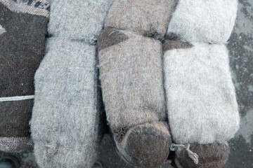 Handmade felt boots displayed on a surface showcase different shades of gray and beige at a market in winter