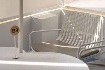 Empty modern outdoor seating area with a white metal chair and table bathed in soft natural light