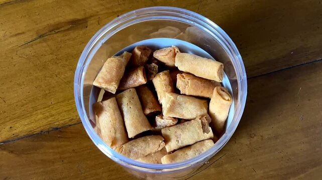 Top view of a transparent jar filled with Sumpia, a small, thin, and crispy Indonesian traditional spring roll. It's filled with dried shrimp (ebi) floss, along with seasonings.