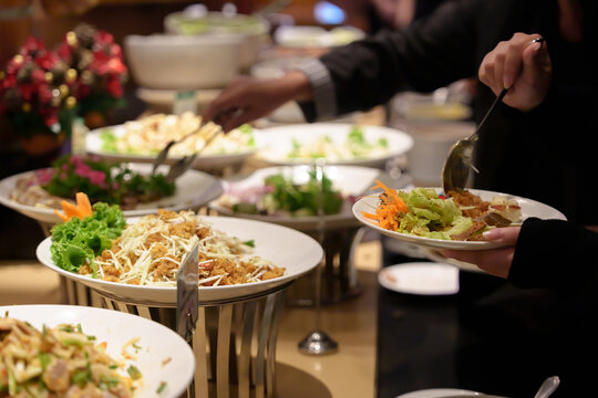 People's hands serving themselves at buffet during party or seminar in hotel, with a variety of food and drinks available.