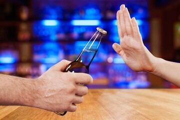 A hand refusing a bottle of beer being offered, set against a colorful bar background, symbolizing choice, moderation, and responsible drinking