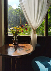 A cozy, inviting corner filled with natural light, a flower vase, and wooden furniture