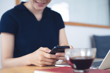 Happy woman using smartphone during working on laptop computer at home office. Asian casual business woman, freelancer remote working, using mobile phone browsing the internet, closeup