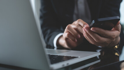Close up, businesswoman using mobile smart phone during working on laptop computer at office. 