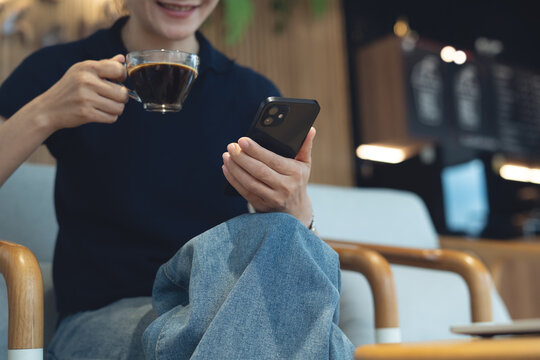 Happy young asian woman using smartphone and drinking coffee, social network at coffee shop. Smiling freelancer using mobile phone video call at cafe, modern people lifestyle