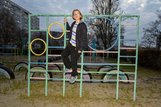 boy in glasses and a jacket stands on a playground in an urban environment in the evening