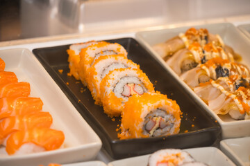 Close-up of assorted sushi rolls on display in a buffet setting including California rolls and various types of nigiri