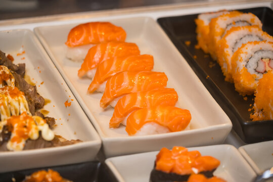 Close-up view of assorted sushi including salmon nigiri, maki rolls, and other Japanese dishes displayed in serving trays - Powered by Adobe