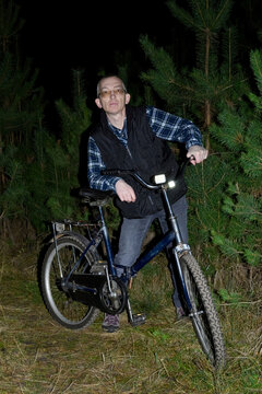 portrait of man with bicycle in night forest looking directly at camera lens