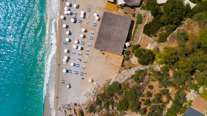 Oludeniz, Turkey. Top down aerial view of pebble beach with rocky cliffs, colorful umbrellas and people sunbathing on shore, turquoise sea waves, summer.. Aerial View