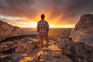 Young woman hiker or tourist is standing at rocky lake bay shore and enjoys sunset view. Khyargas Nuur lake, Mongolia