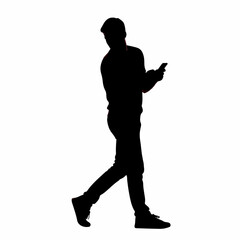 Silhouette of a young man walking while looking at his smartphone.