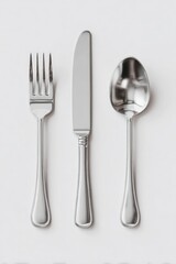 Overhead shot of a fork, knife, and spoon; polished, metallic, arranged vertically on a light gray background