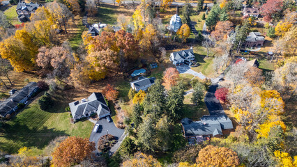 Symmetrical aerial shot of suburban community in Newburgh NY during fall. Dense trees with orange tones, roads curving around homes, and soft lighting highlight suburban tranquility.