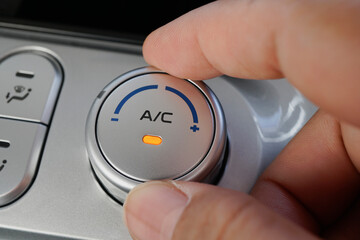 A person adjusting the air conditioning control in a vehicle, with a focus on the dial and indicator light.