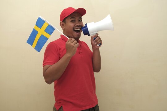 Southeast Asian man holding Swedish flag and megaphone, promoting visa, scholarship, or study abroad opportunities in Italy; isolated with copy space for advertisement.